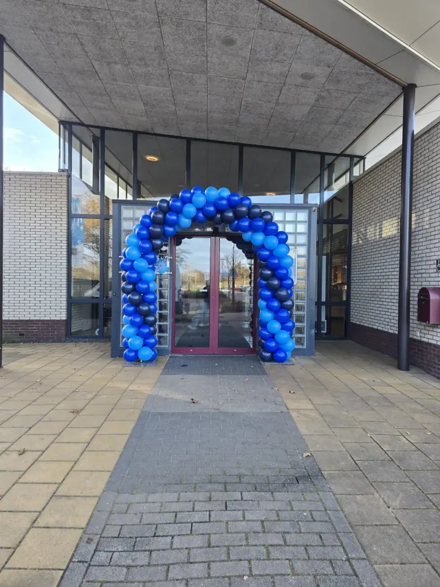 Blauwe ballonnenboog rond een entree van een bedrijfsgebouw