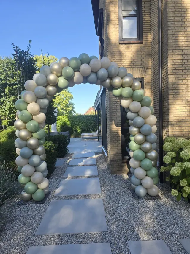 Grote ballonnenboog in saliegroen, wit en zilver in een tuin