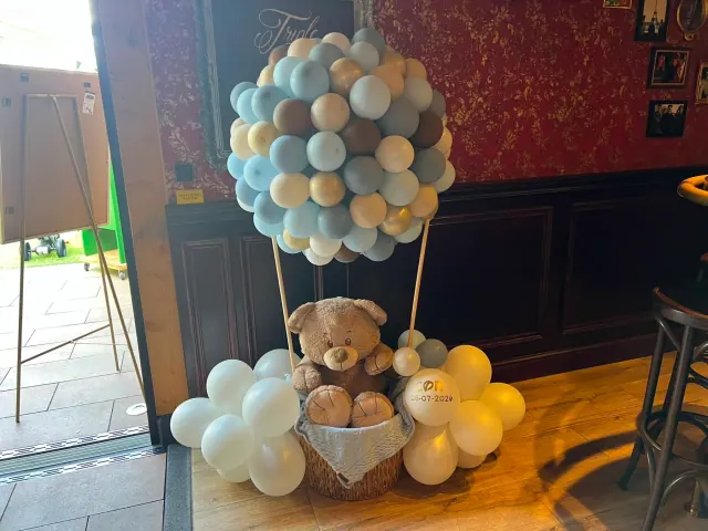 Teddybeer in een mand onder een wolk van blauwe en beige ballonnen